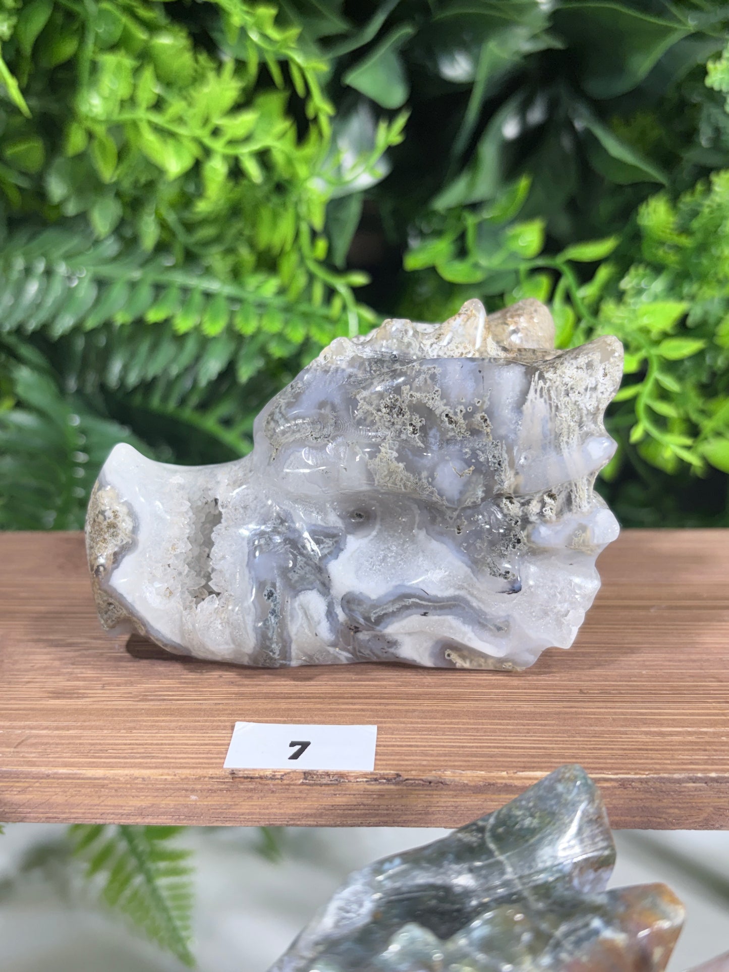A natural agate crystal cluster with gray and white bands, mounted on a wooden display stand with a small white label marked '7'.