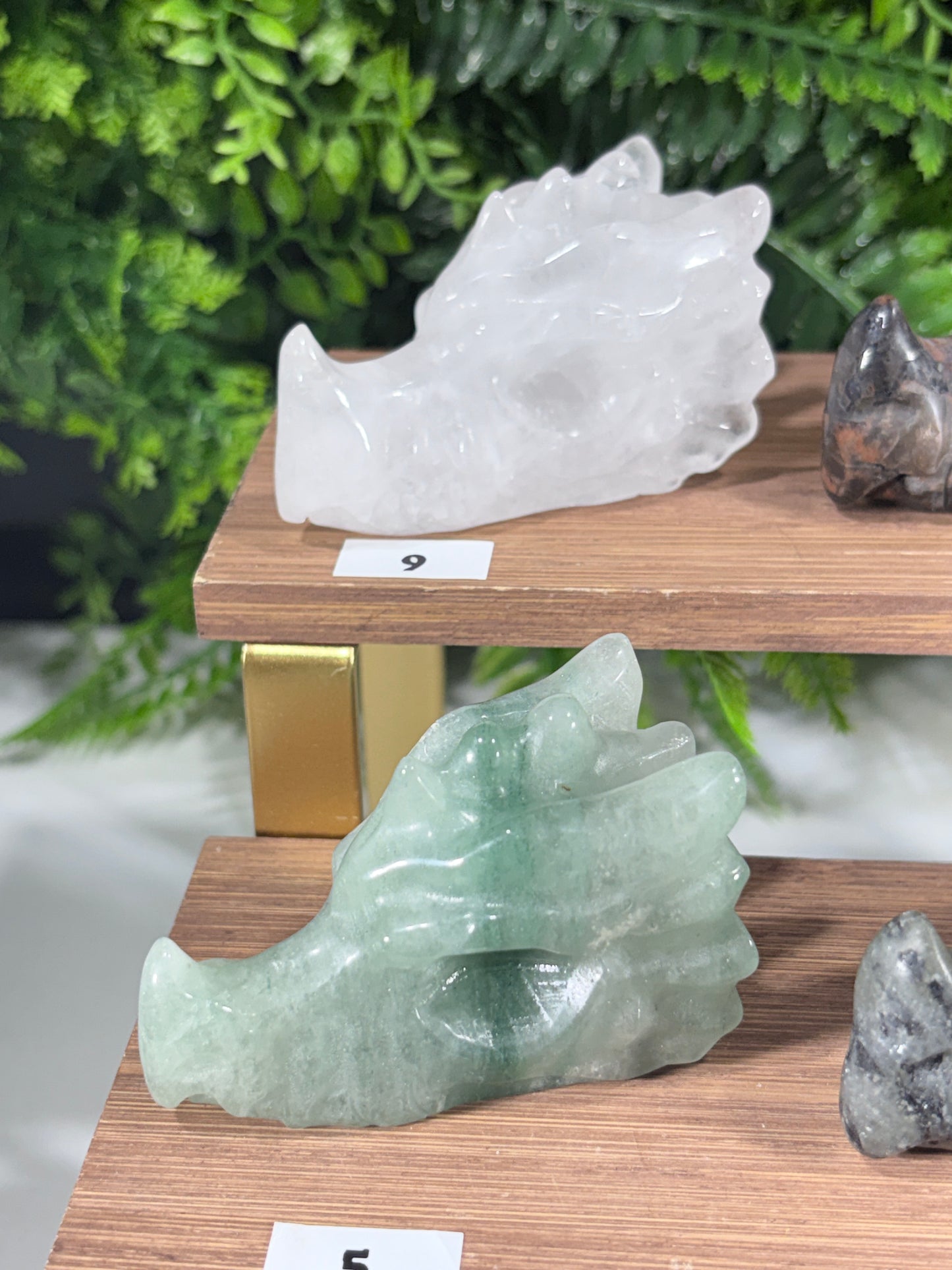 Three wooden display stands holding multiple polished crystal dragon figurines in various colors, set against a green foliage backdrop.