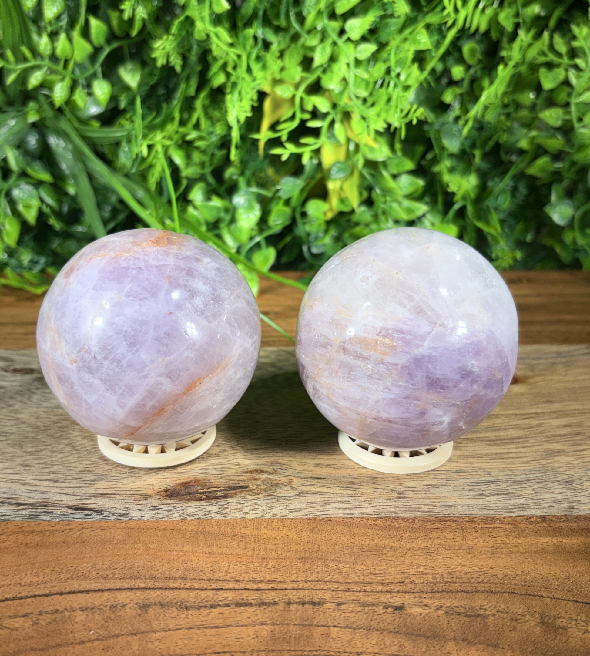 Two spherical amethyst crystal wall lights mounted on a rustic wooden panel next to a green foliage background.