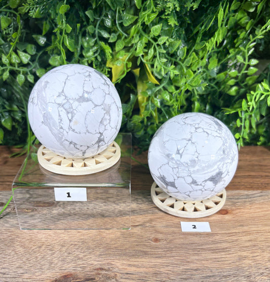 Two spherical stone lamps with white and gray marbled patterns, mounted on circular wooden bases, displayed on a rustic wooden surface next to green foliage.