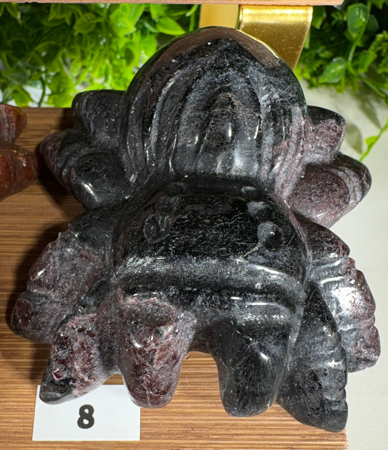 A carved dark stone spider with a glossy, polished finish, displayed on a wooden surface with a small white card showing the number 8.