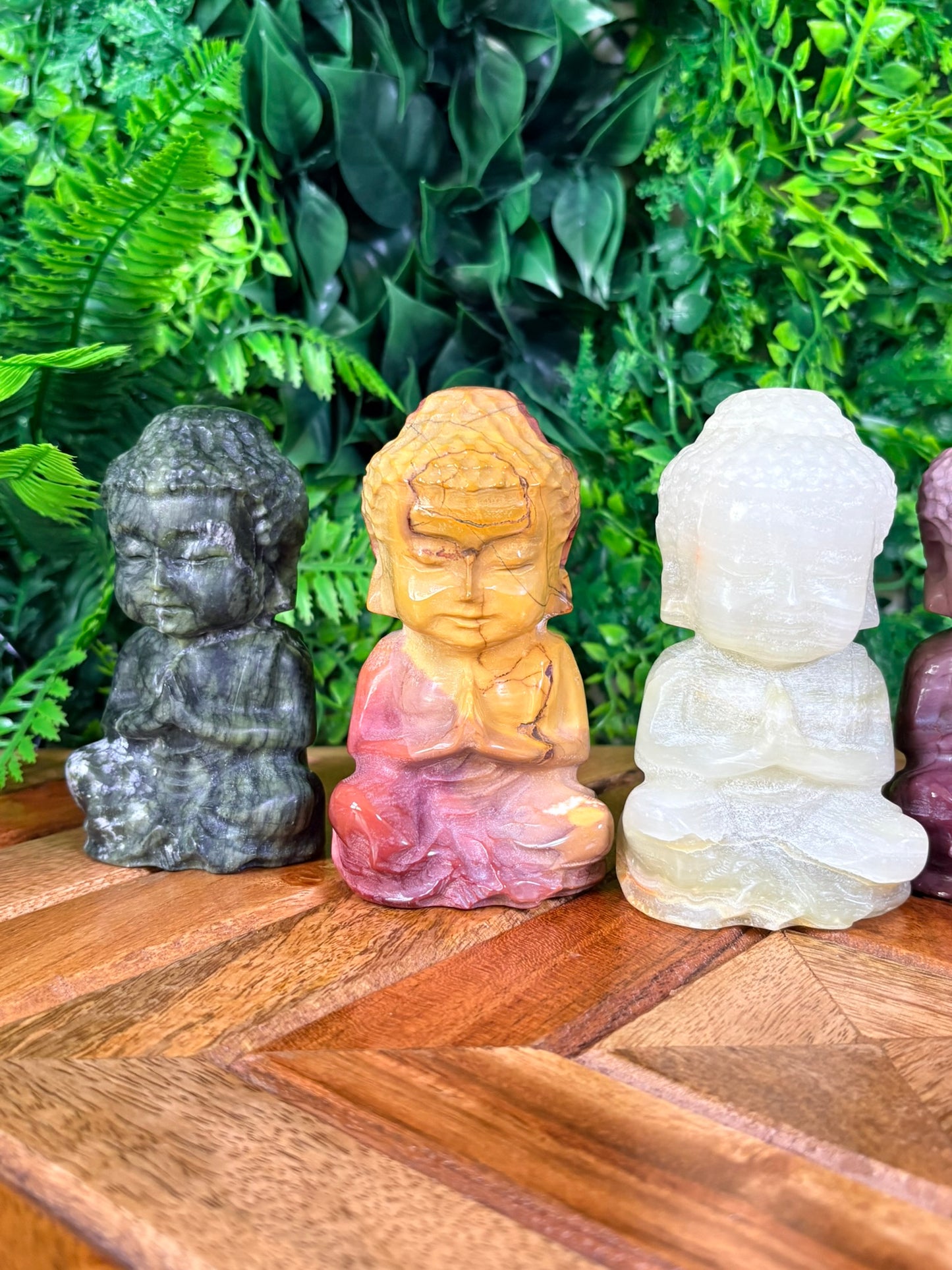 Set of stone Buddha statues on a wooden surface with green foliage in the background
