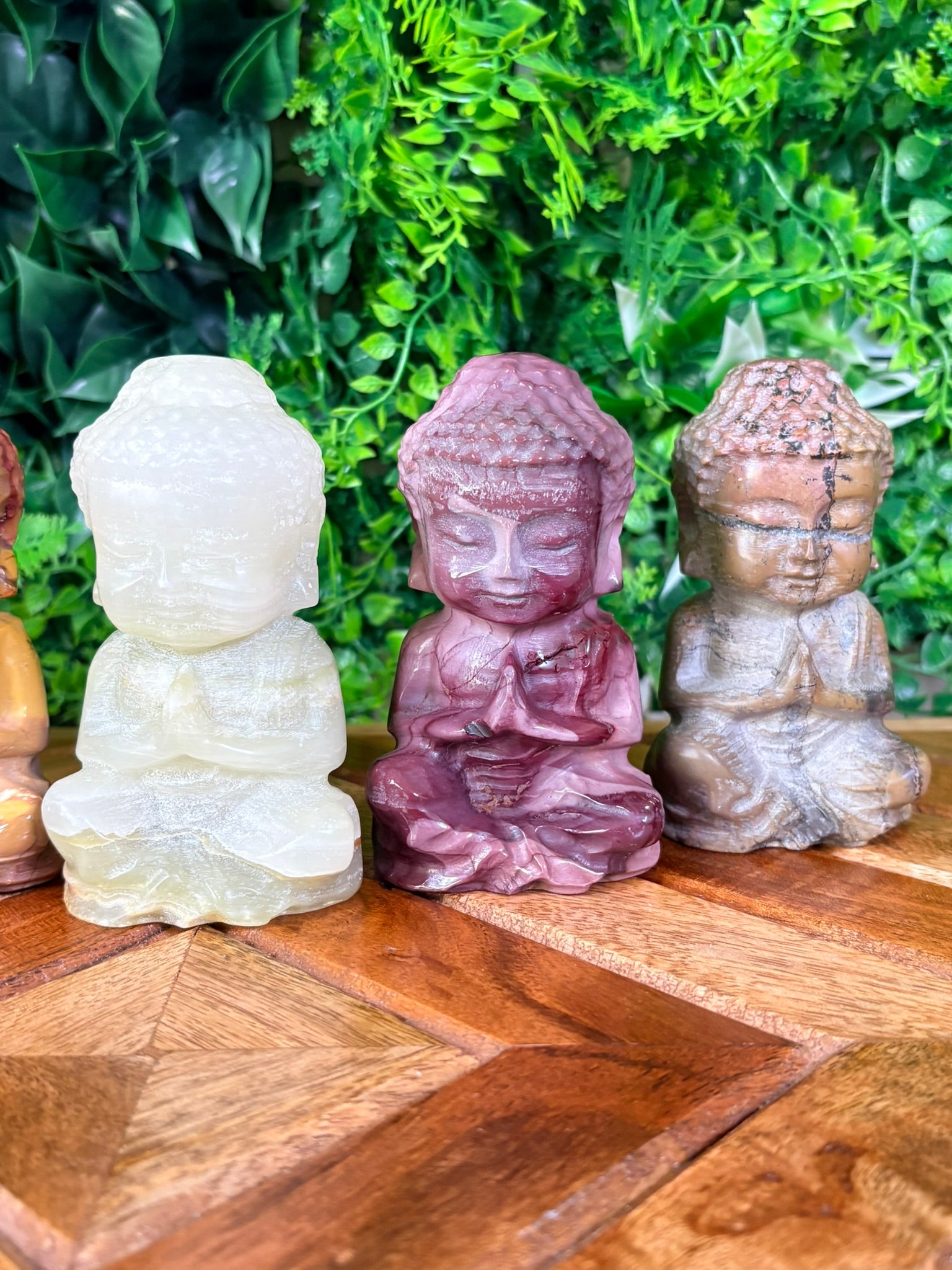 Set of four stone Buddha statues on a wooden surface with a green leafy background
