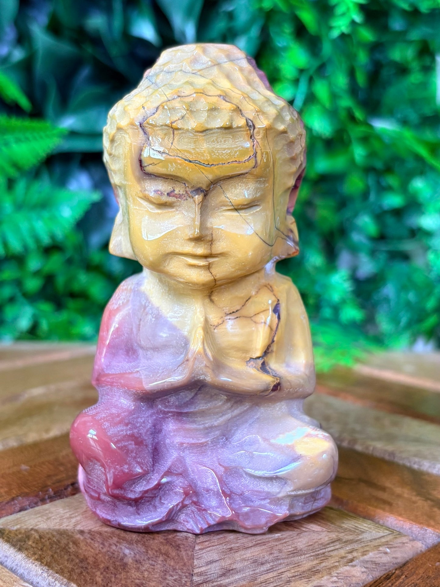 Carved stone statue of a meditating figure on a wooden surface with green foliage in the background