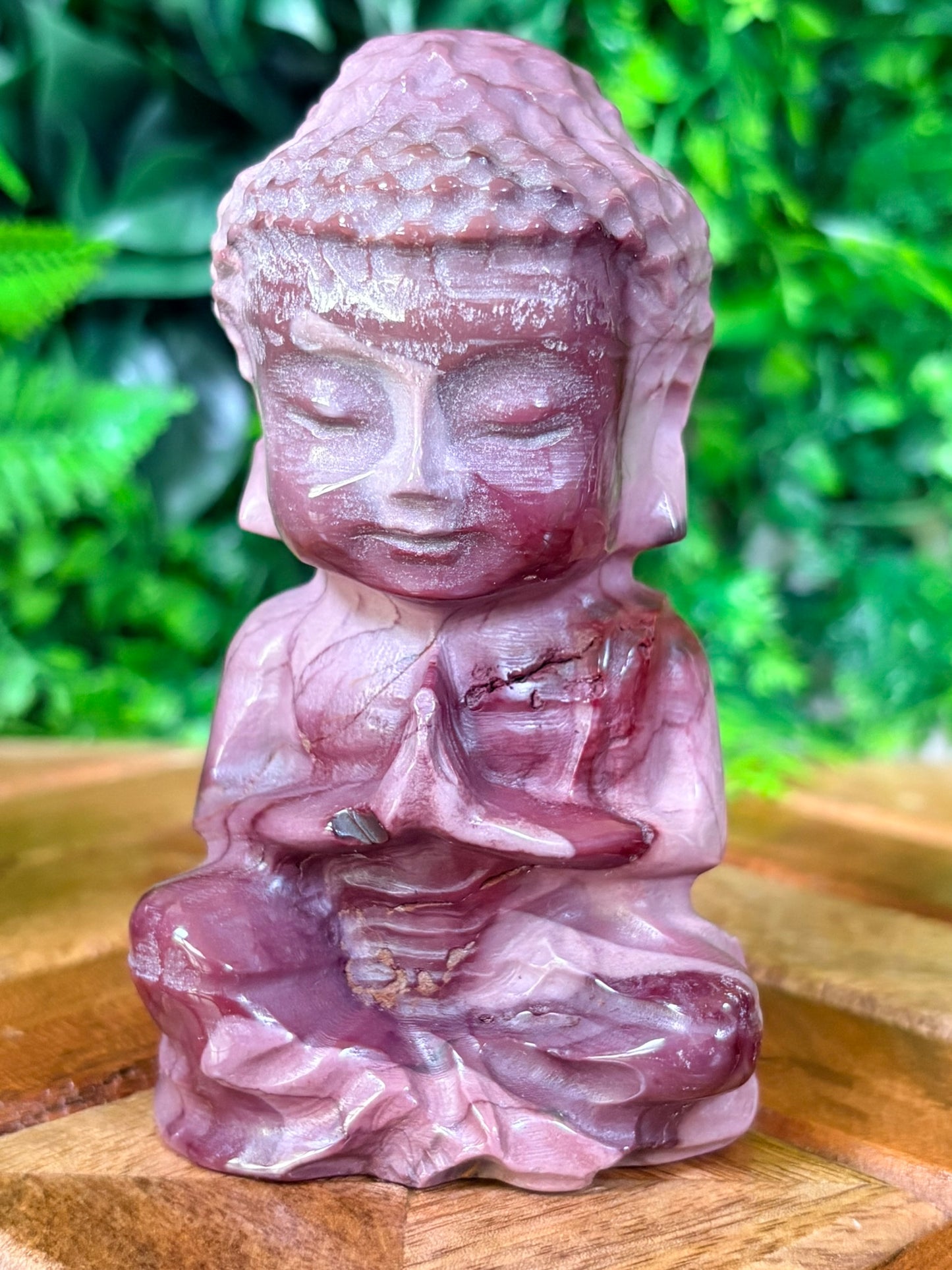 Pink stone Buddha statue on a wooden surface with a green leafy background